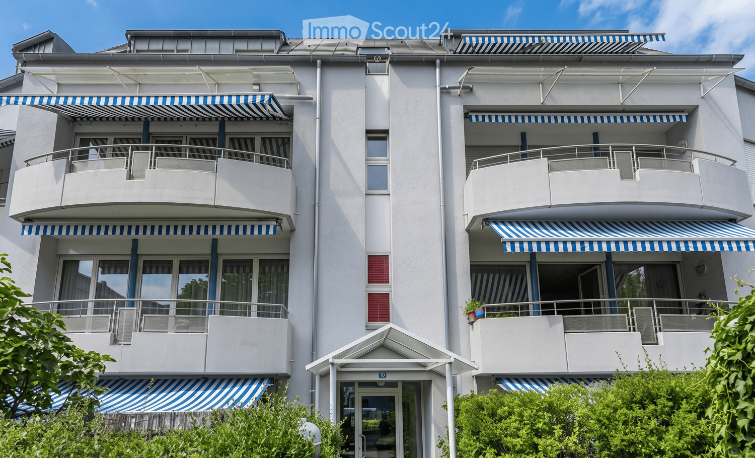 Modern multi-story residential building with white exterior, multiple balconies with blue and white striped awnings, and potted plants on some balconies.