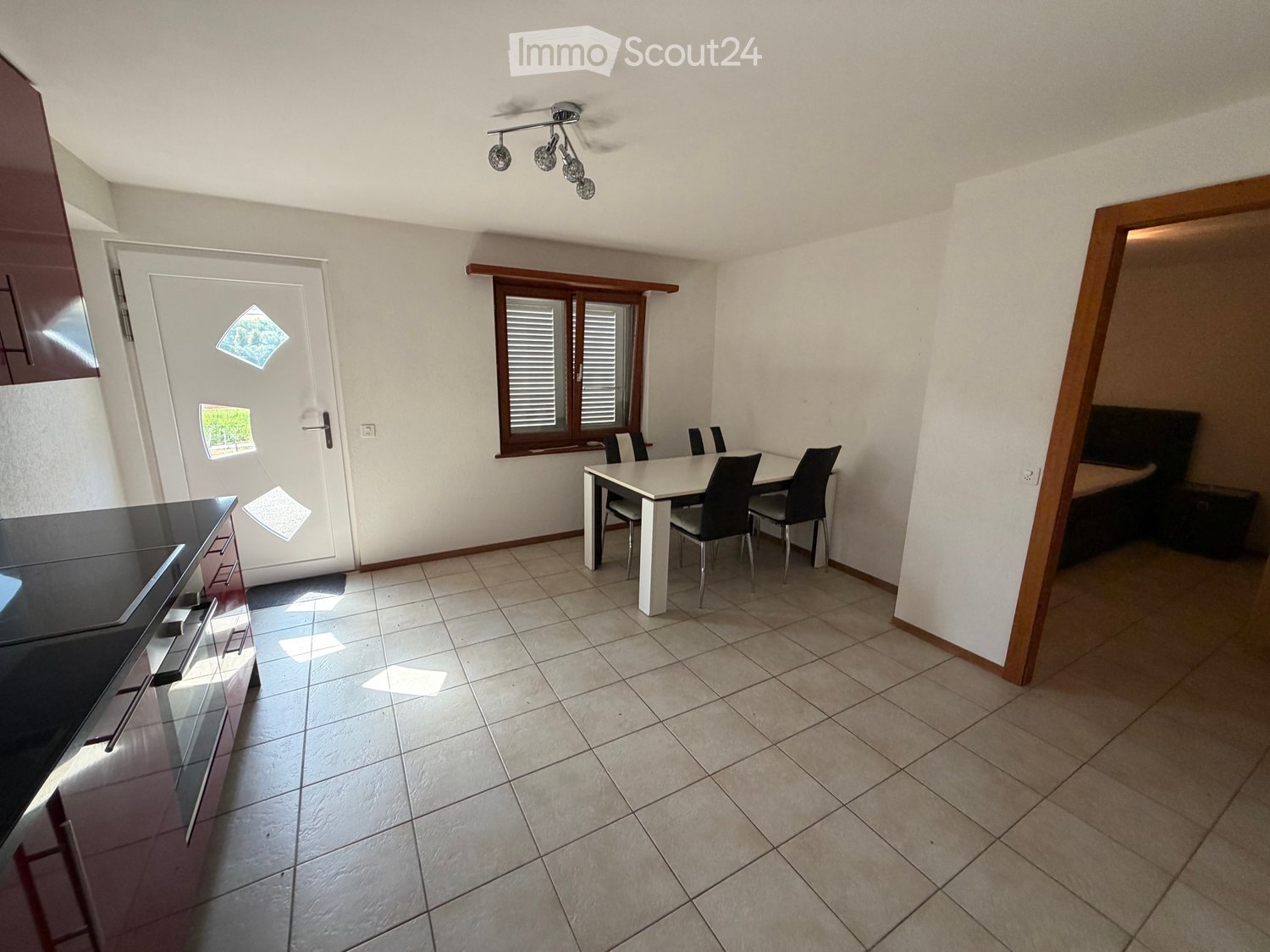 Open-plan kitchen and dining area with tiled flooring, white dining table, four chairs, and dark kitchen cabinetry.