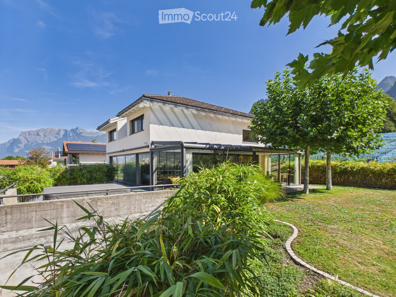 Modern two-story house with white exterior, large windows, and a spacious garden with well-maintained lawn and greenery.