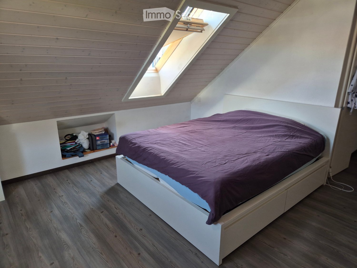 Cozy attic bedroom with wooden walls and floor, featuring a built-in bed with storage drawers and a built-in shelf for books and items.