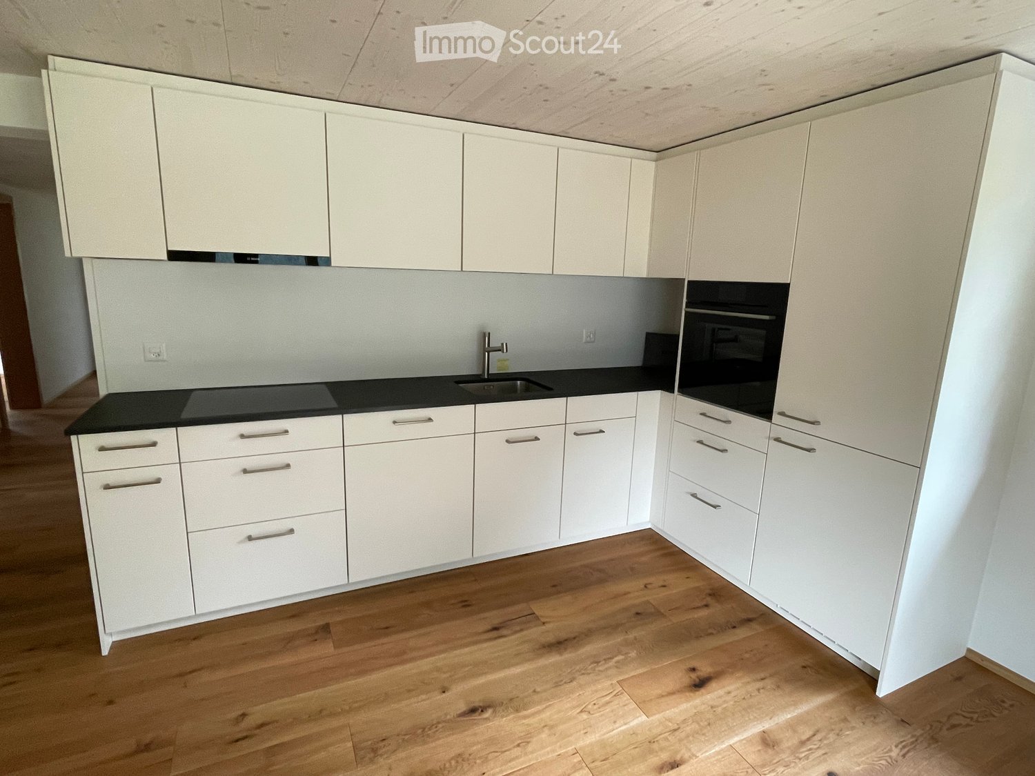 Modern kitchen with white cabinets, black countertops, and wooden flooring.