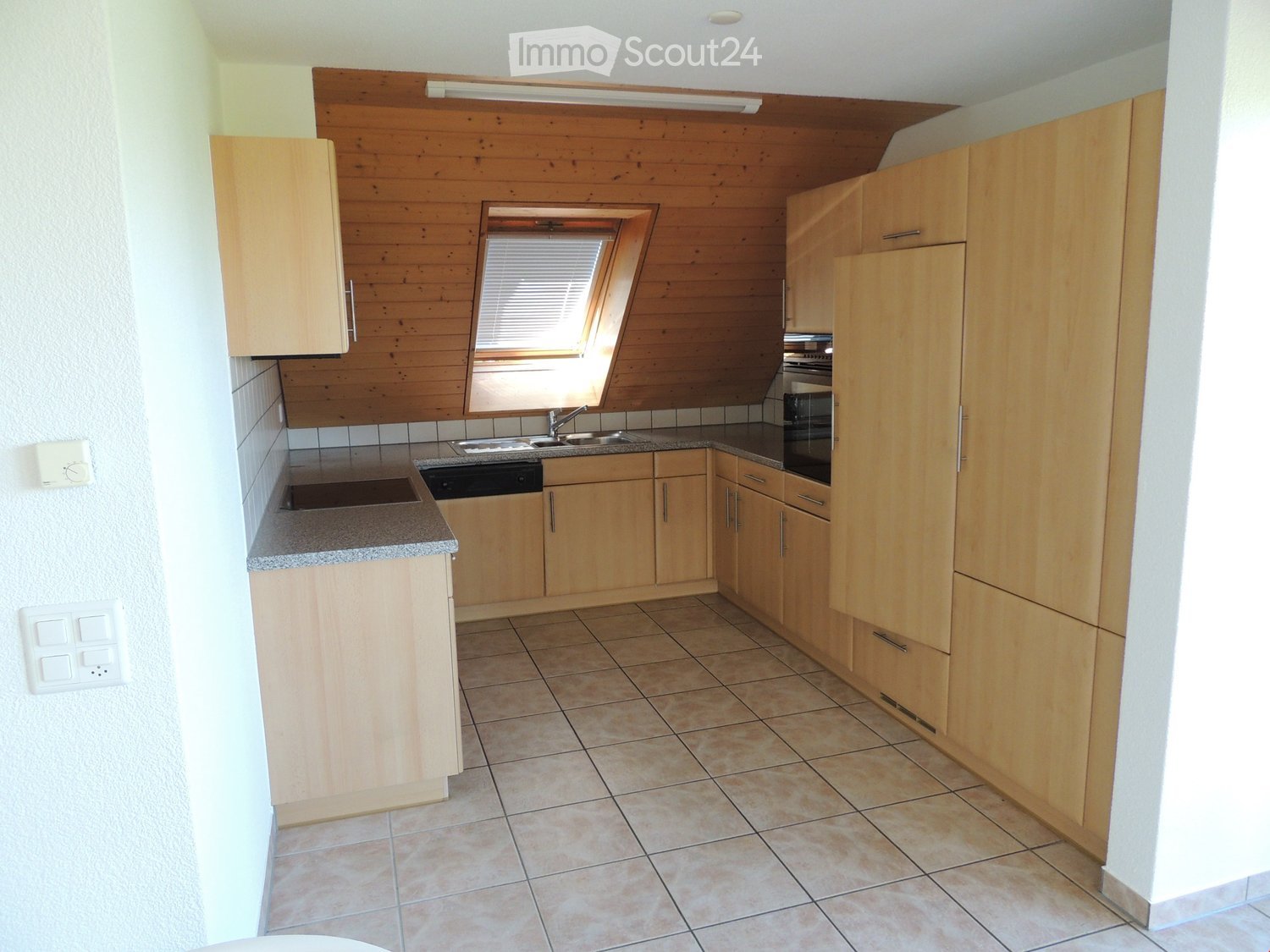 Modern kitchen with light wooden cabinets, granite countertops, tiled floor, and built-in appliances including an oven and dishwasher.