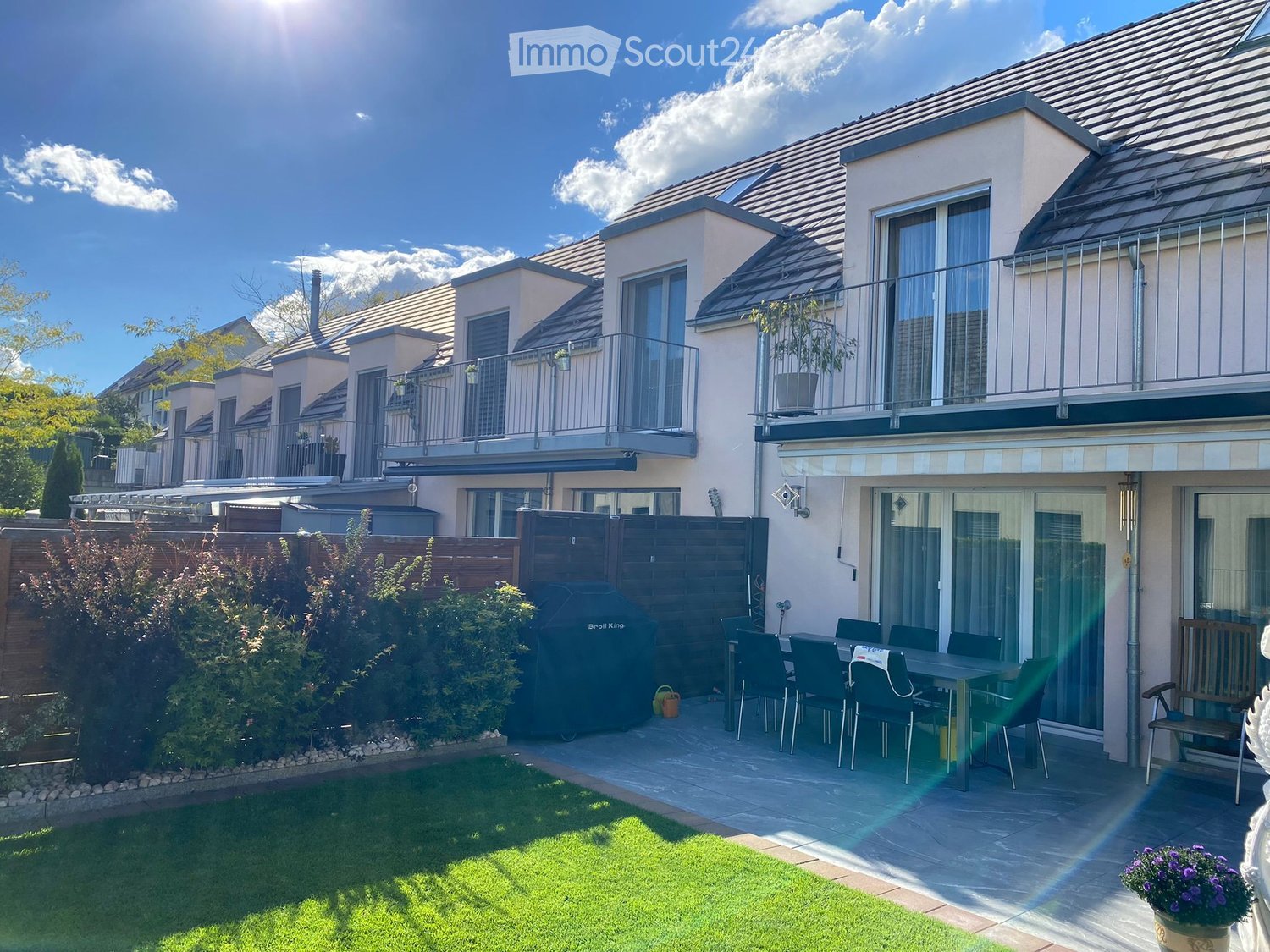Well-maintained garden with a patio area, outdoor dining set, grill, and potted plants.
