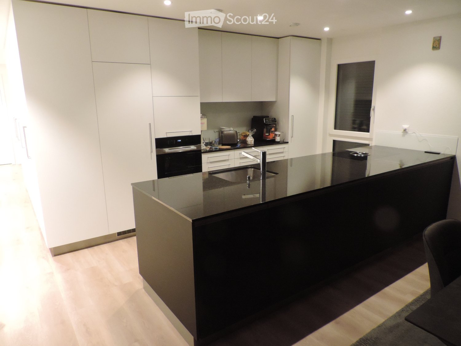 Modern kitchen with white cabinets, black countertops, stainless steel sink, and various appliances including an oven, toaster, and coffee maker.