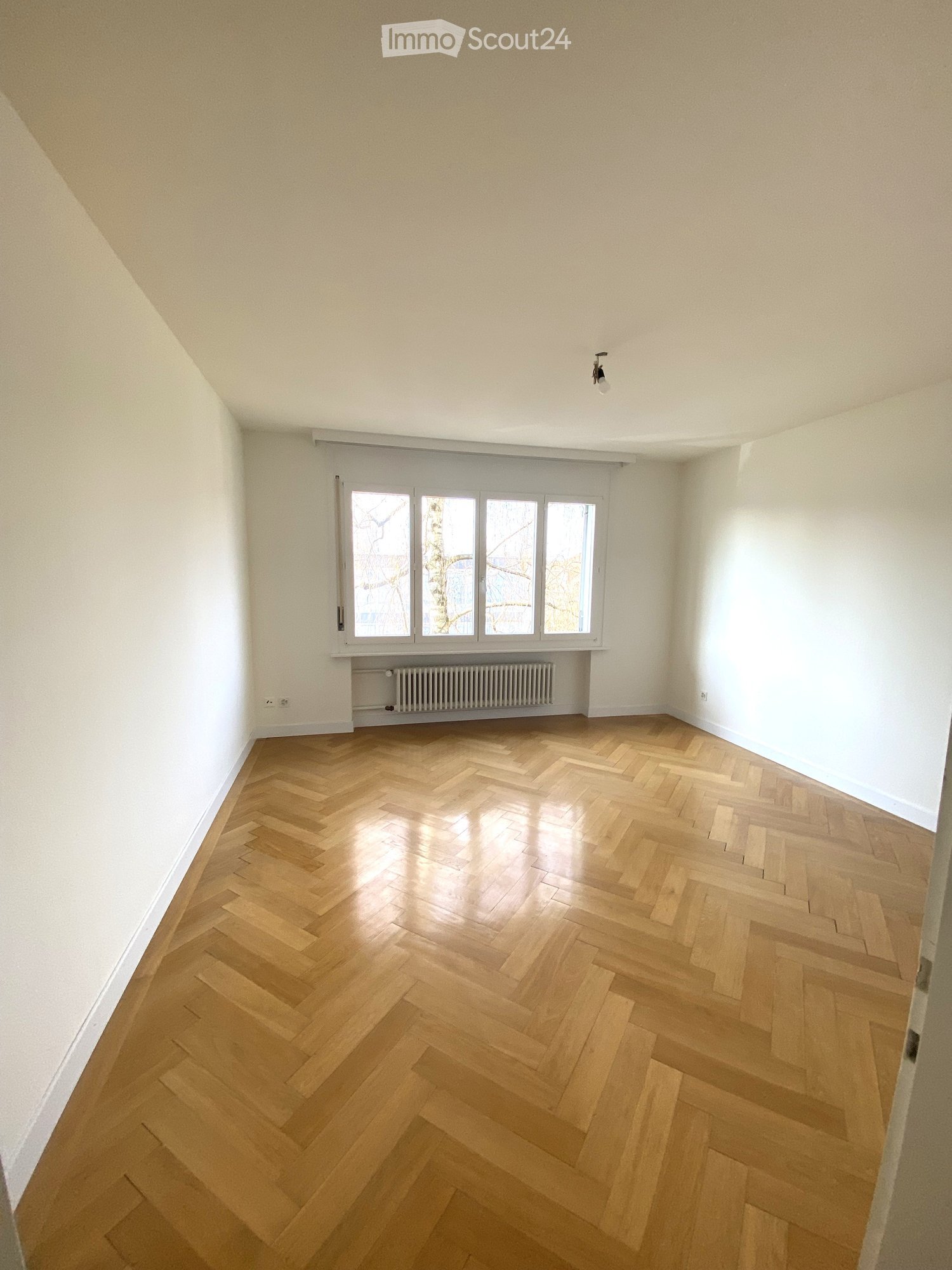 Empty room with wooden floor, white walls, windows with radiators, no furniture