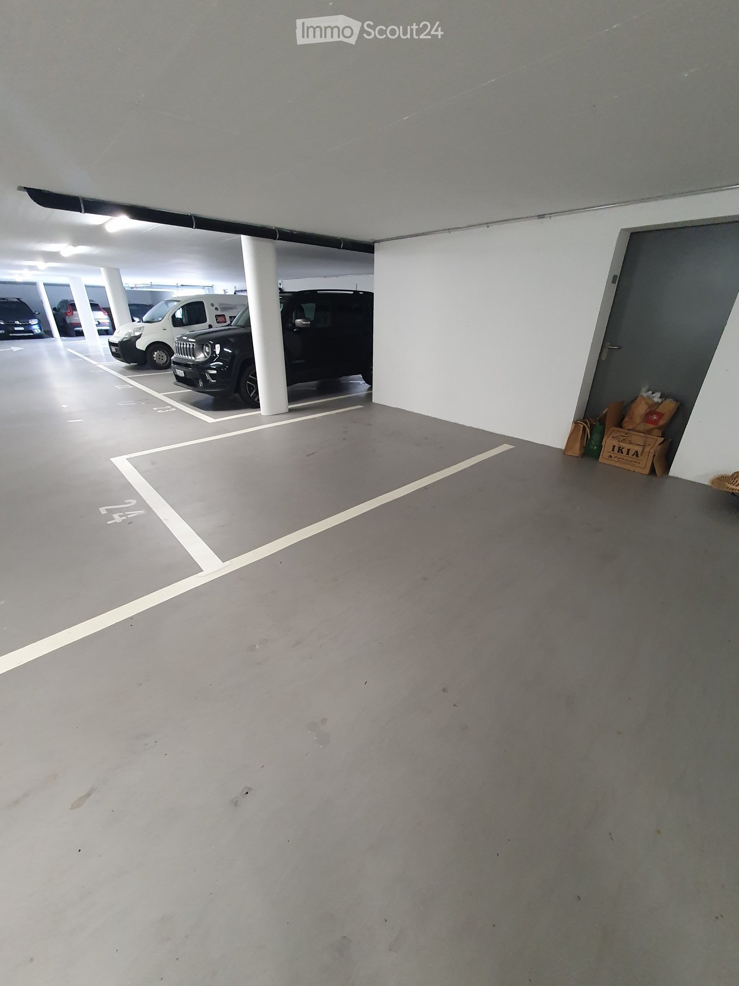 Underground parking area with several parked cars, white pillars, and marked parking spaces.