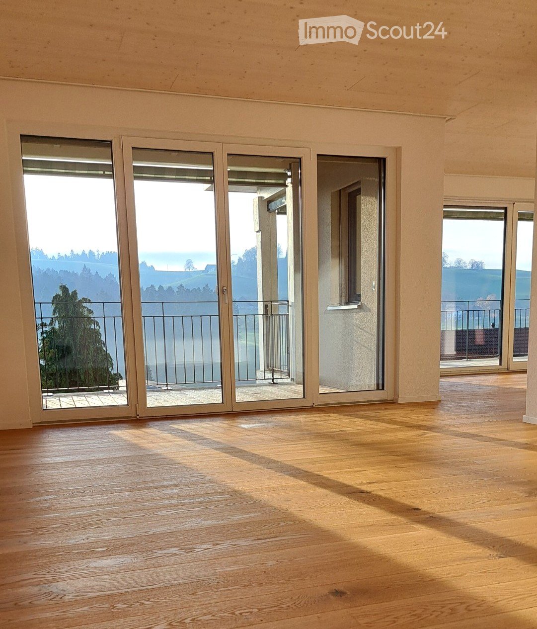 Empty room with wooden flooring and large sliding glass doors leading to a balcony with a scenic view.
