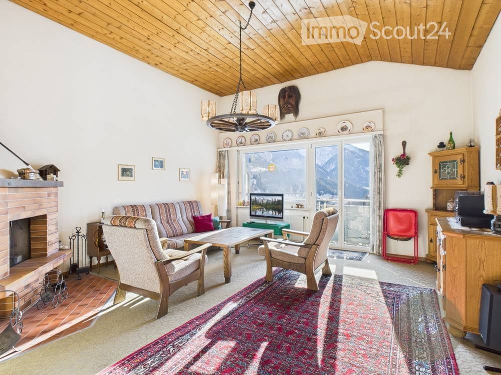 Cozy living room with a fireplace, large window offering a mountain view, sofa, armchairs, coffee table, television, and decorative items.