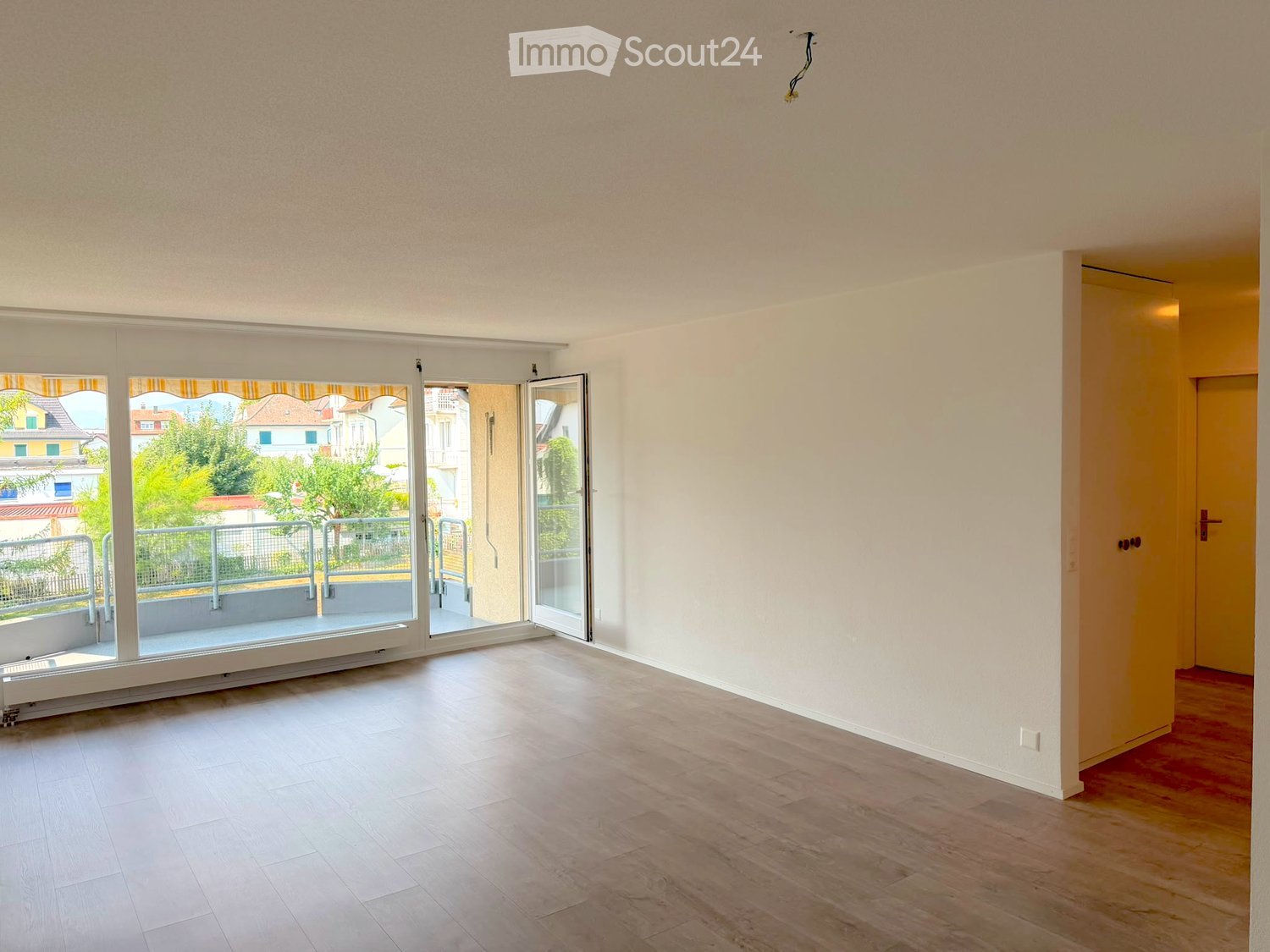 Empty room with light-colored walls, wooden flooring, and large sliding glass doors leading to a balcony.