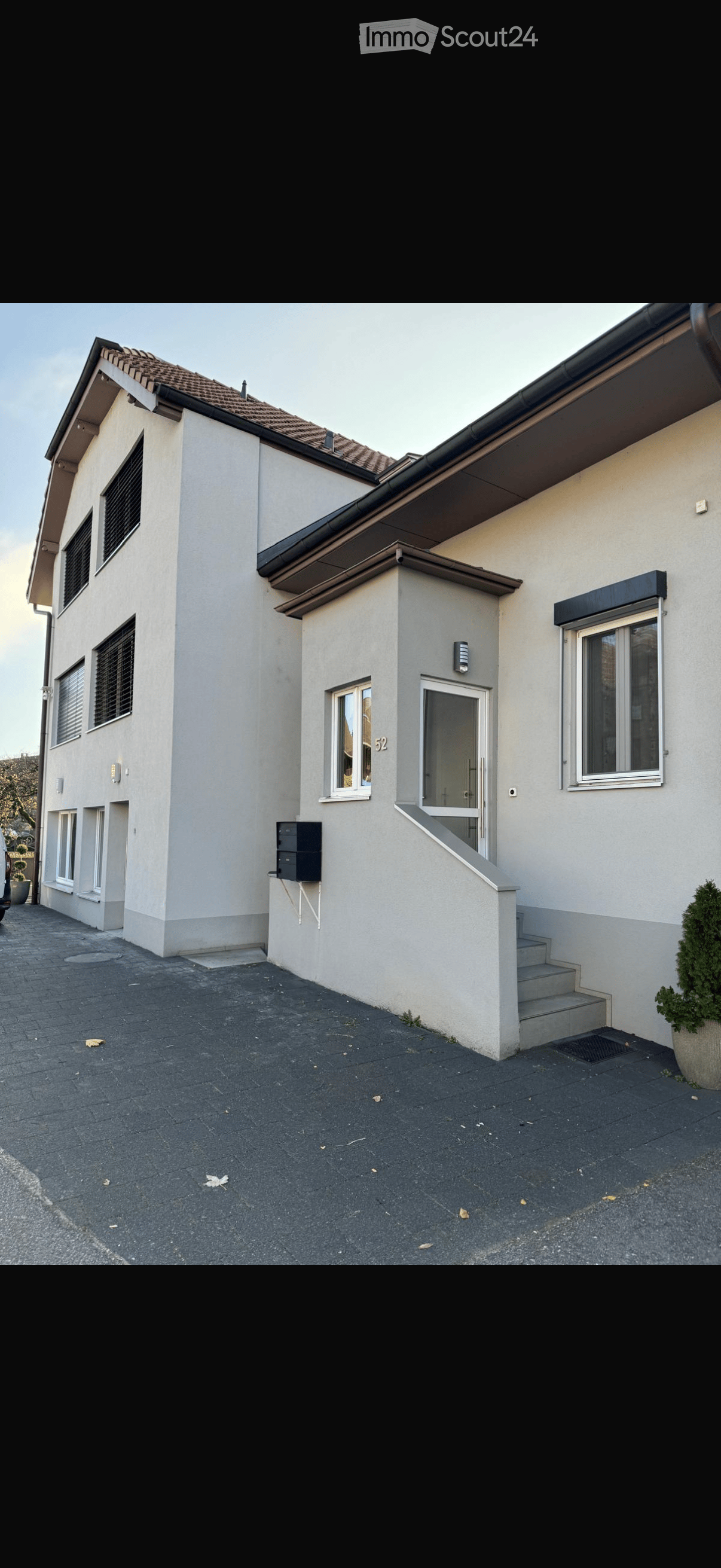 Two-story house with beige exterior, tiled roof, multiple windows, and a small staircase leading to the entrance.