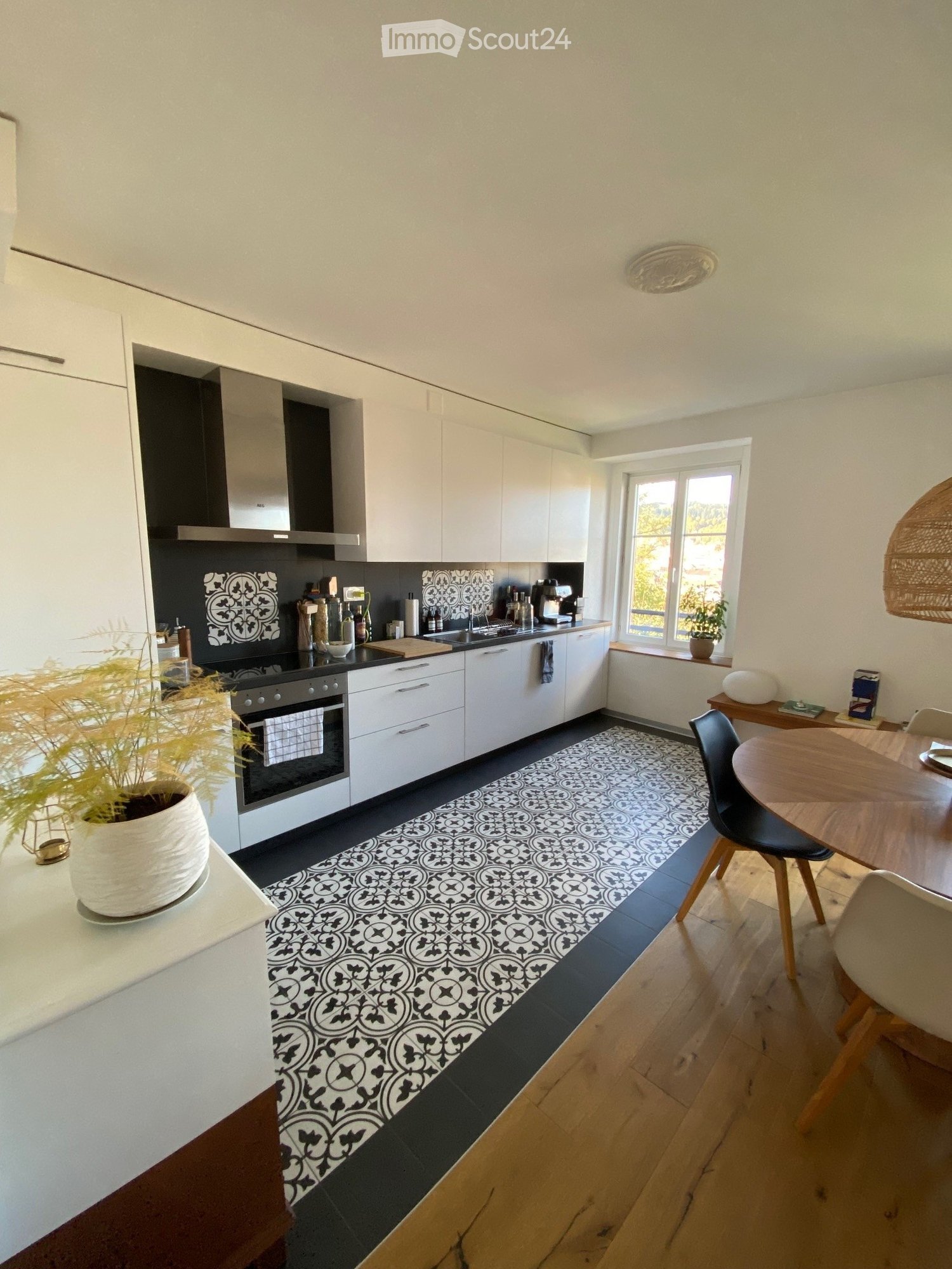 open plan kitchen and dining area, white cabinets, black countertop, black and white tile flooring, dining table and chairs, window
