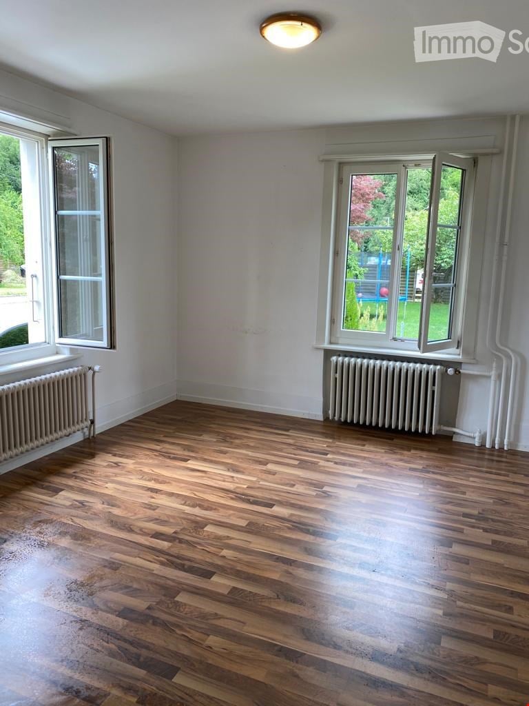 Empty room with wooden flooring, white walls, large windows, and radiators.