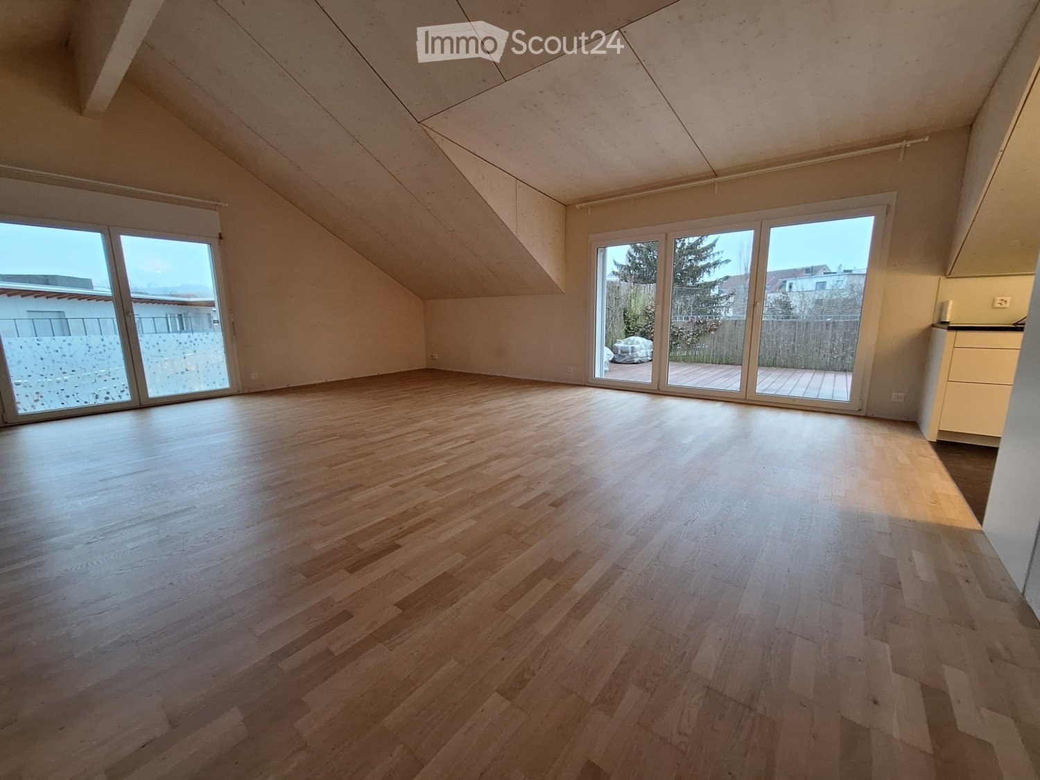 Empty attic room with wooden flooring, large windows, and sliding doors leading to a terrace.