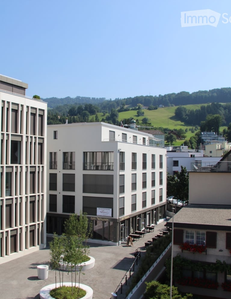 modern white building, multi story, several balconies, greenery on facade, raised ground floor, outdoor seating, green slopes in background