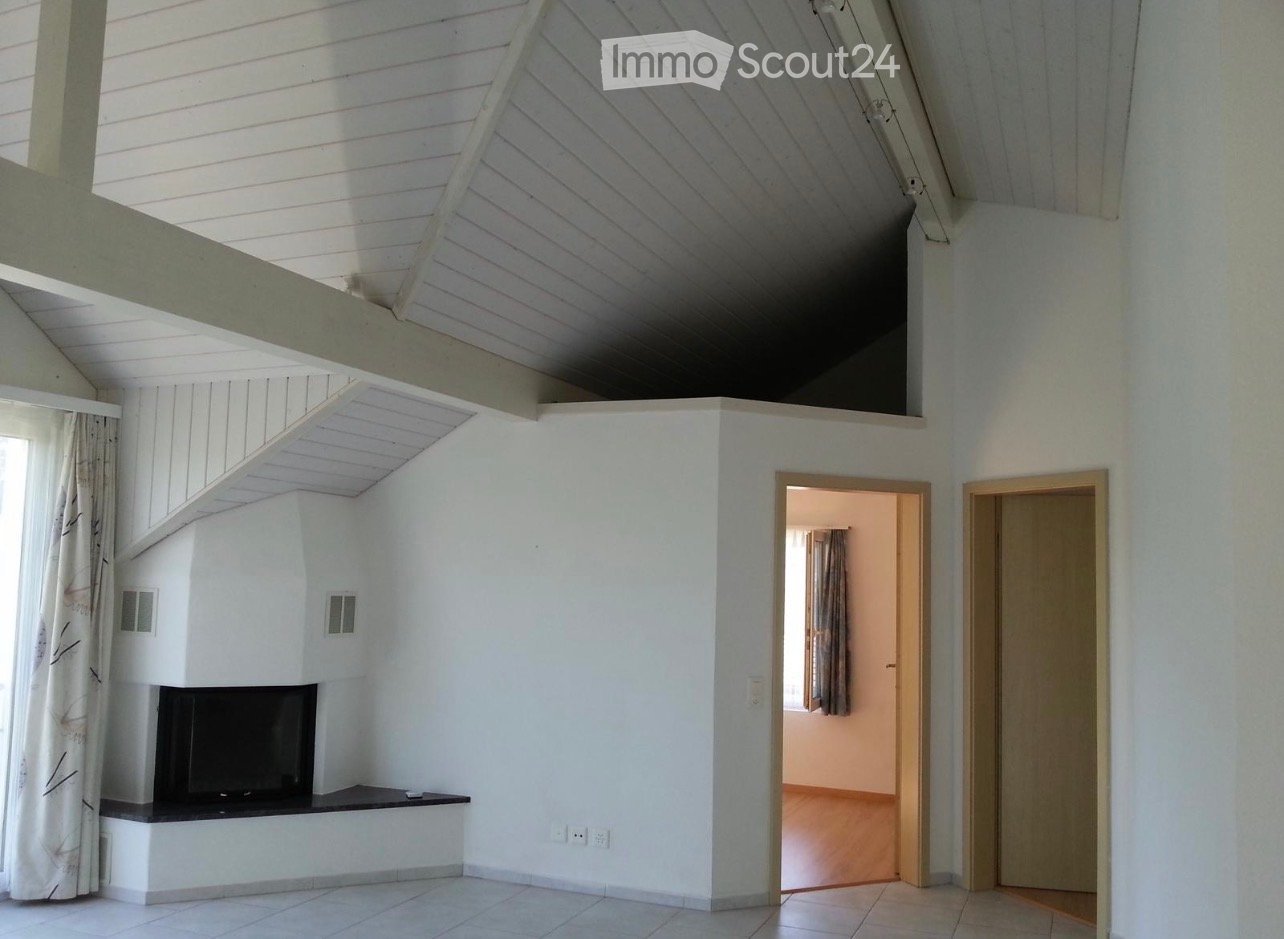 Bright living room with white walls, tiled floor, fireplace, and a large window with curtains. The room features an open staircase leading to an upper level.