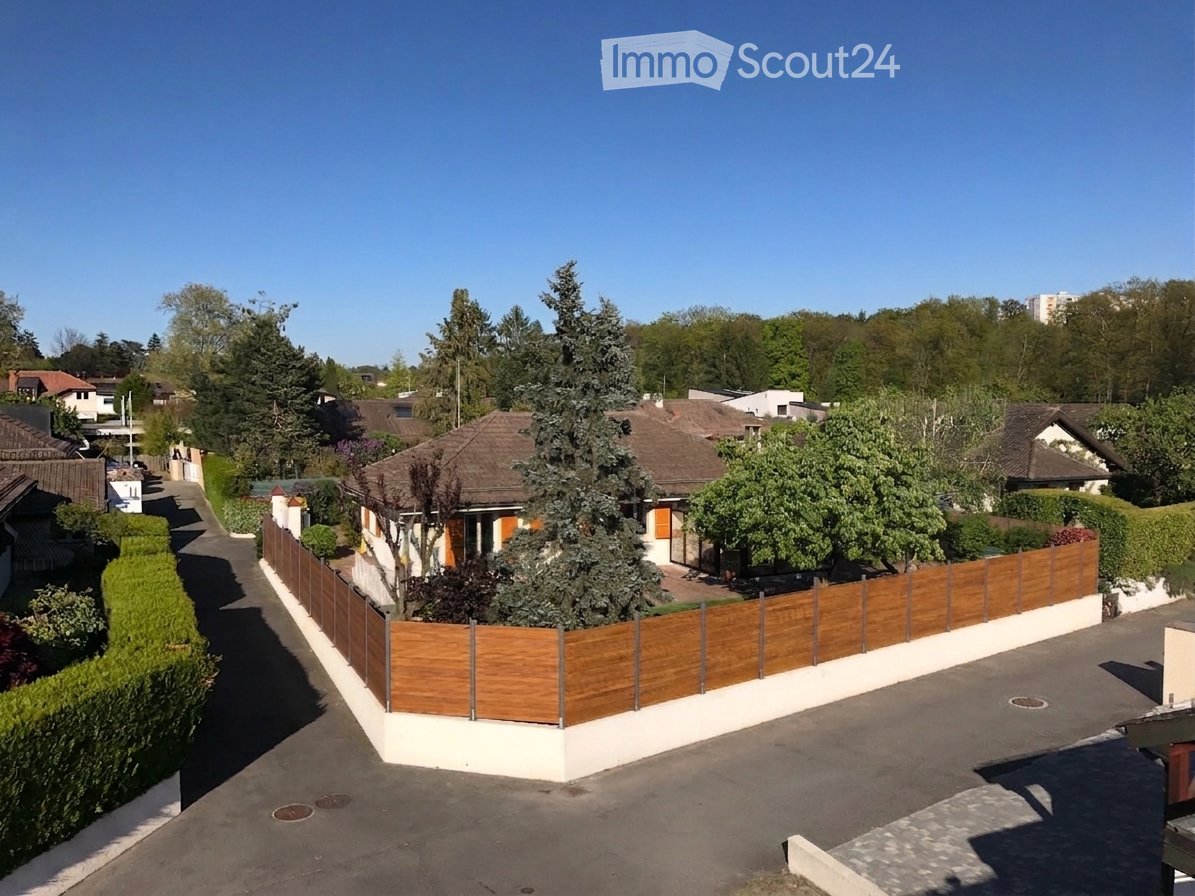 A two-story house with a brown tiled roof, surrounded by a wooden fence and trees, located in a residential neighborhood.