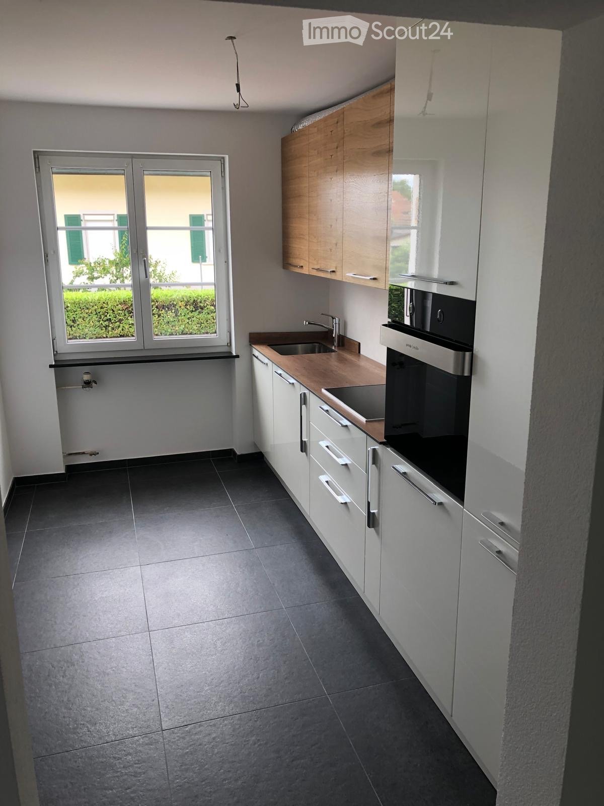 Modern kitchen with white cabinets, wooden countertops, stainless steel sink, and built-in oven. Large window provides natural light.
