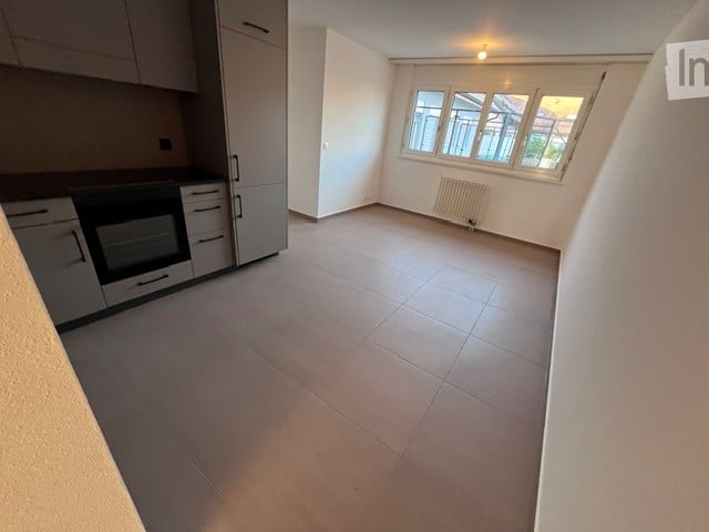 Empty room with tiled floor, white walls, and a window with multiple panes. The room is unfurnished, showing only the basic structure and a radiator under the window.