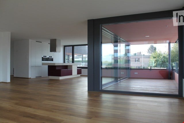 Modern, open-plan kitchen and living area with wooden flooring, large glass sliding doors leading to a balcony, built-in cabinets, and a central kitchen island.