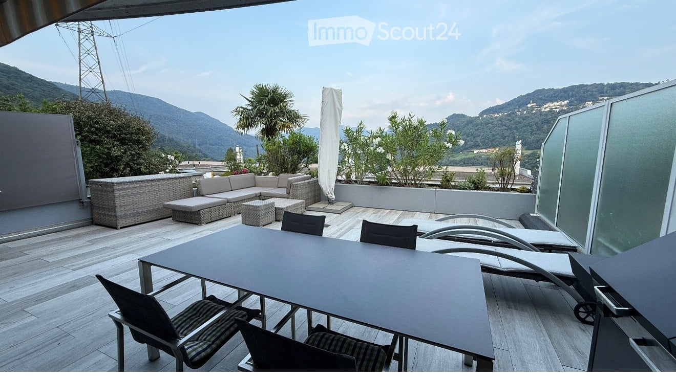 A modern outdoor terrace with a panoramic mountain view, featuring a sofa, coffee table, dining table, chairs, and lounge chairs.