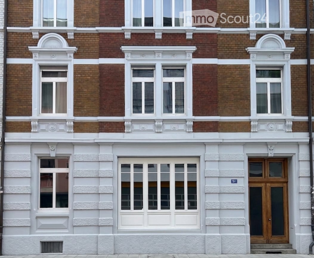 Classic European building facade with red brick upper levels and white plaster lower level, featuring multiple windows with decorative white surrounds and a central wooden door.