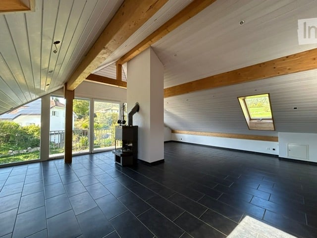 Bright, open room with exposed wooden beams, large windows, and a tiled floor. The space is completely empty, with no furniture or equipment visible.
