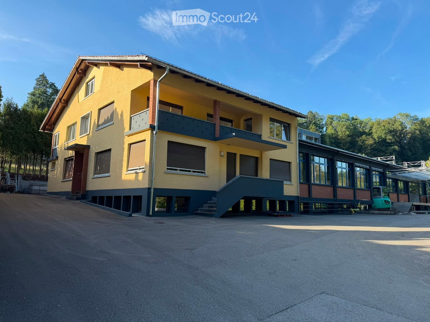 Two-story yellow building with a raised ground floor, multiple windows, and a balcony on the upper level.