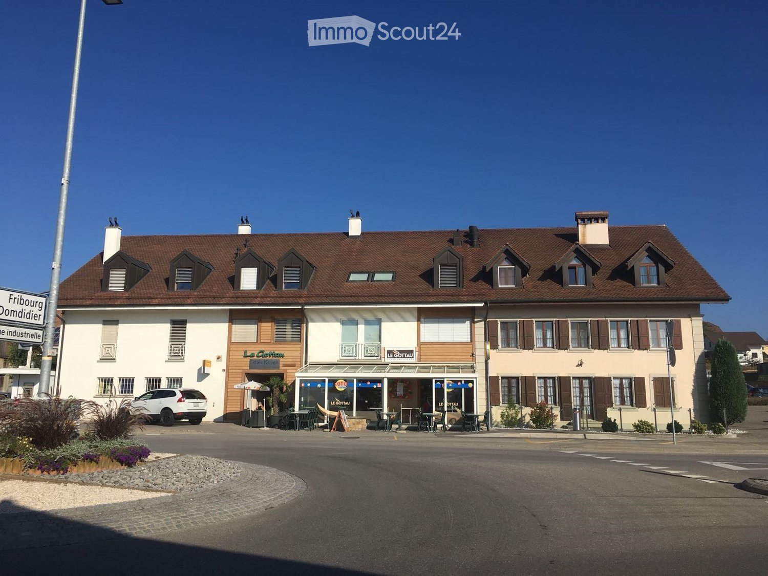 Two-story building with a brown tiled roof, multiple chimneys, and a restaurant area with outdoor seating and tables.