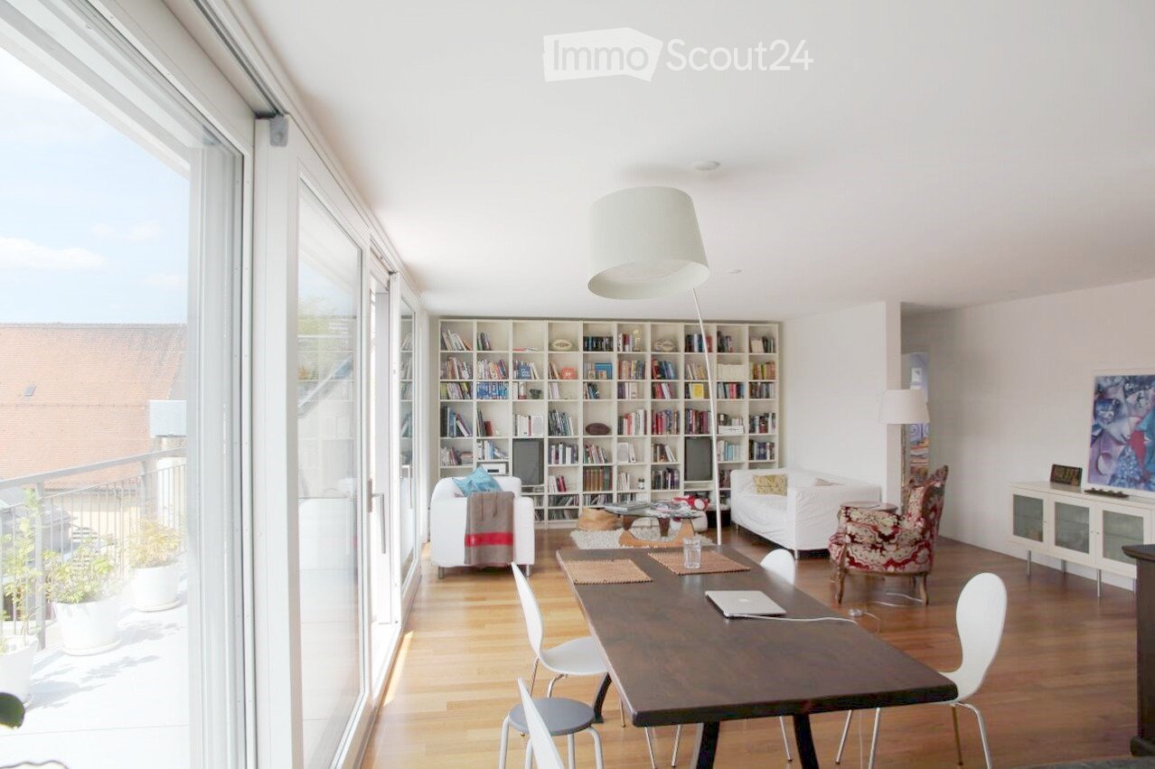 Bright living room with large windows and balcony access, featuring a wooden floor, white sofa, bookshelf, dining table, and modern decor.