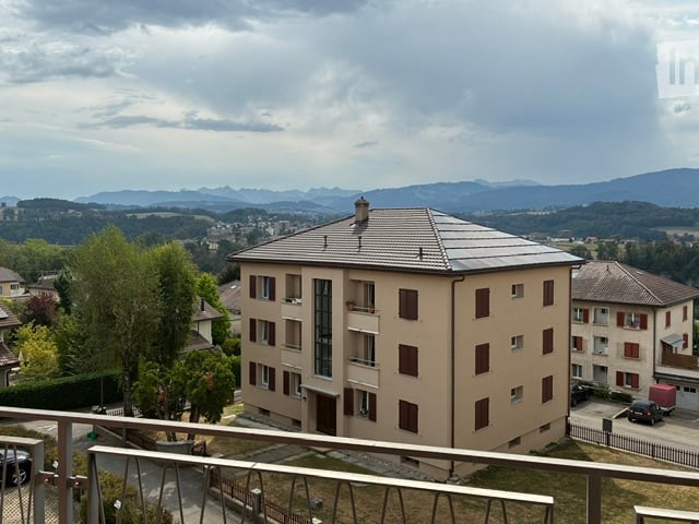 Multi-story residential building with balconies and large windows, overlooking a scenic valley and distant mountains.