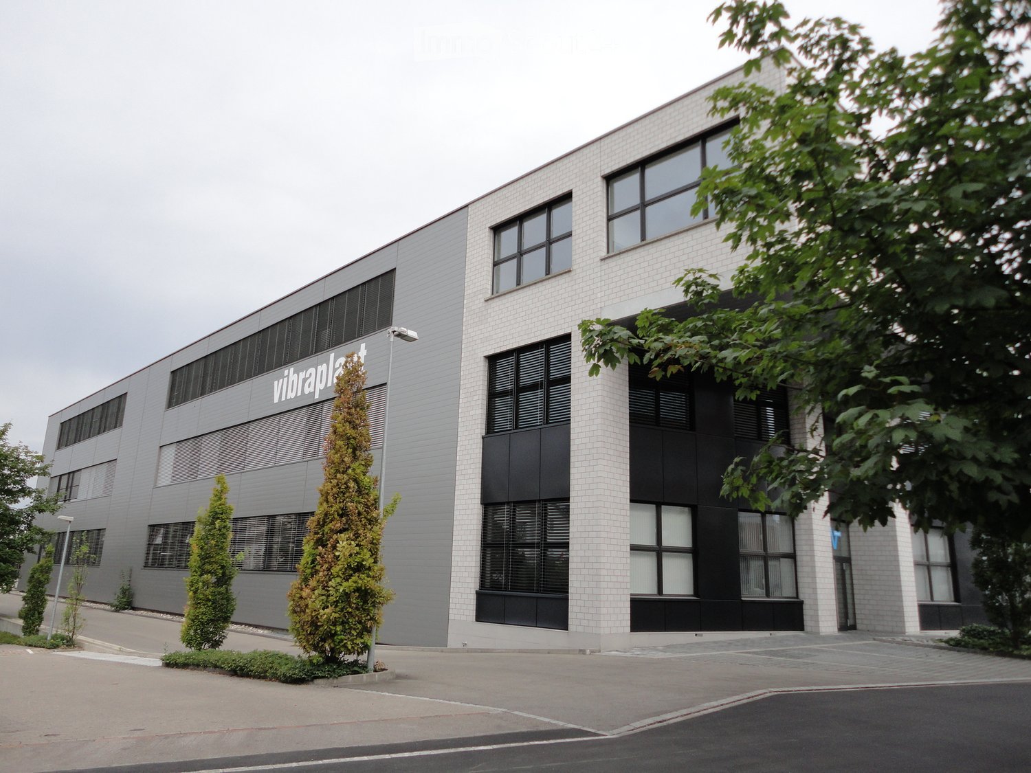Modern two-story building with white brick facade, large windows, and a sign reading "vibraplast".