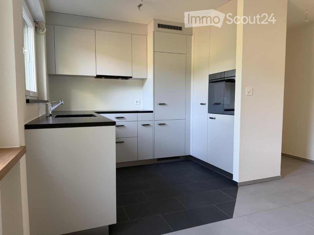 Modern kitchen with white cabinets, black countertop, stainless steel sink, and built-in oven. Dark tiled floor and light-colored walls.