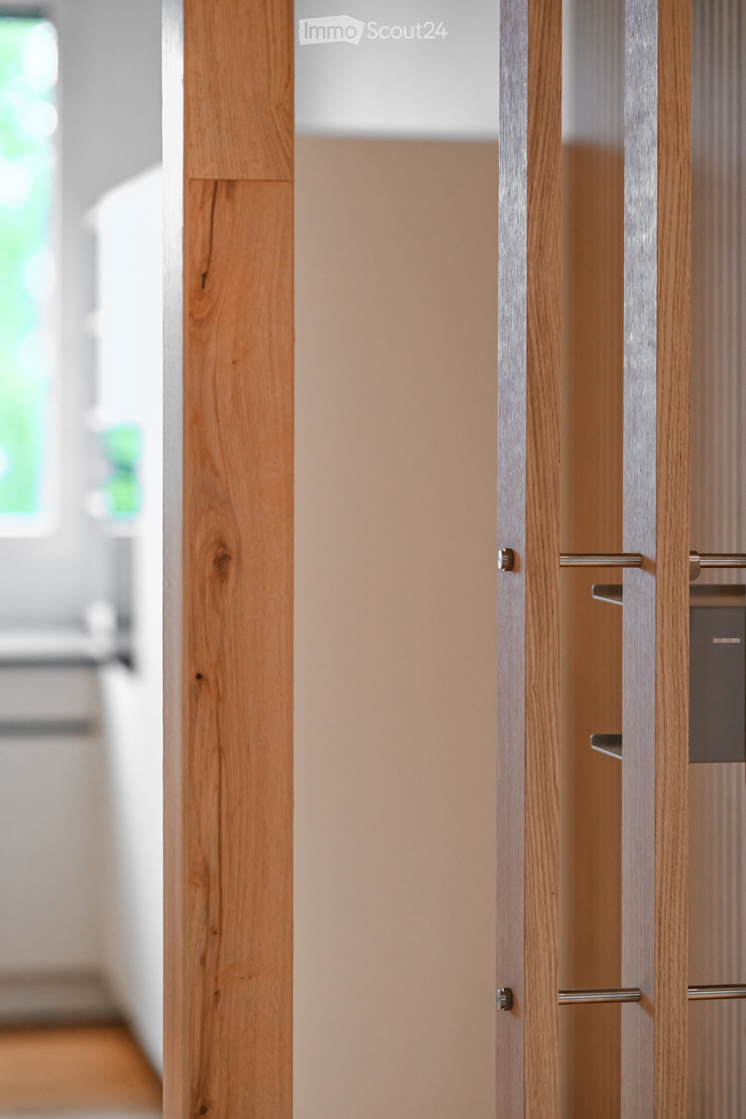 A modern wooden door with a sleek, metallic handle is partially open, revealing a light-colored interior wall and a glimpse of a room beyond.