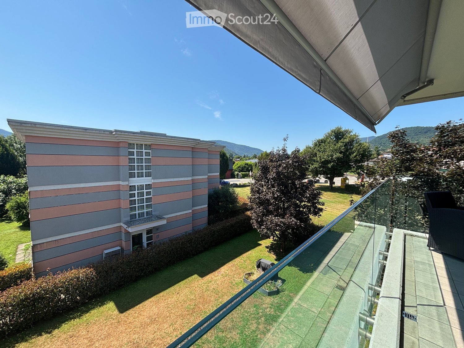 Apartment building, balcony with glass railing, landscaped garden, tree, lawn, distant mountain view