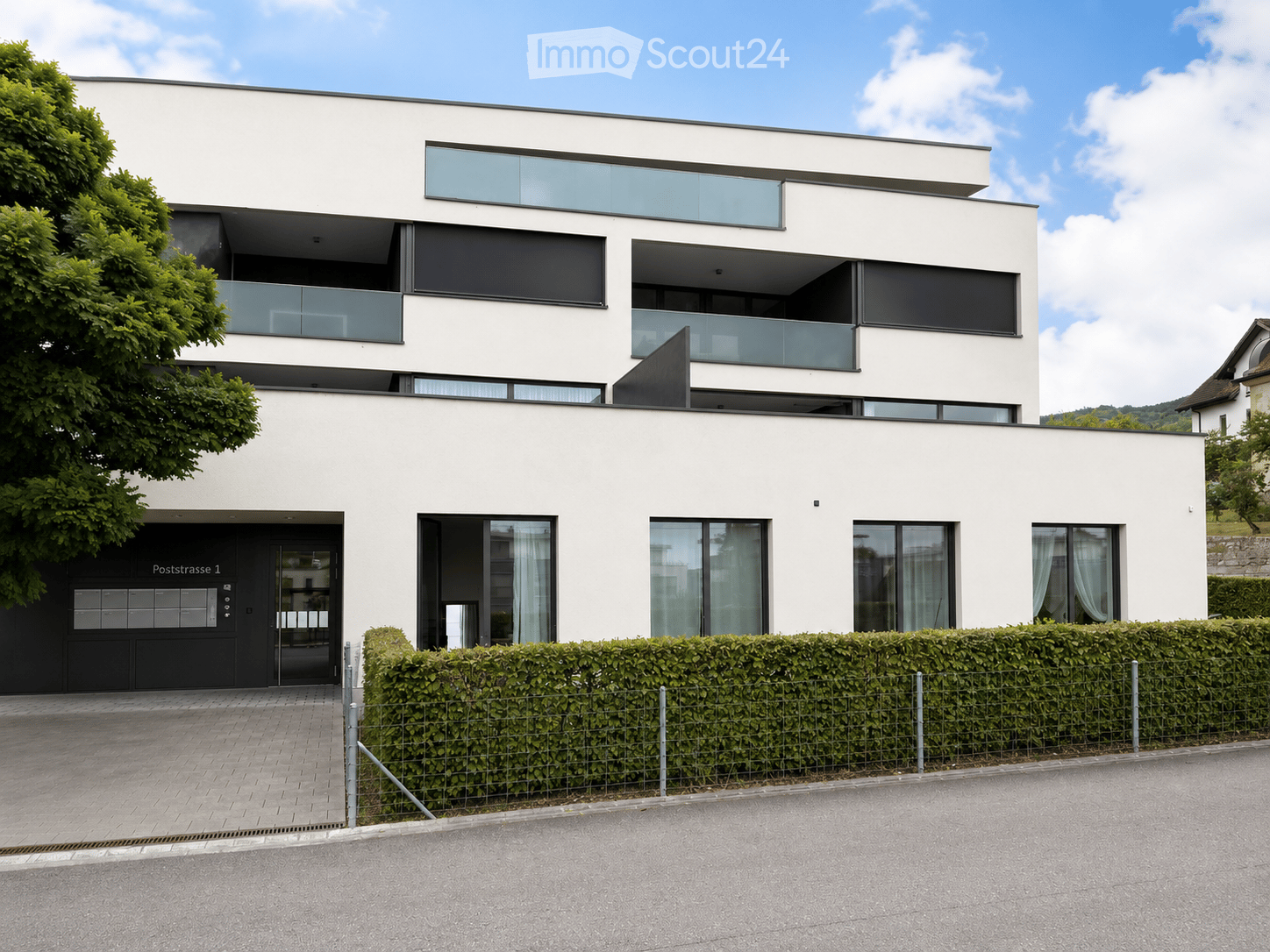 Modern two-story house with white facade, large windows, balconies, and a black entrance door.