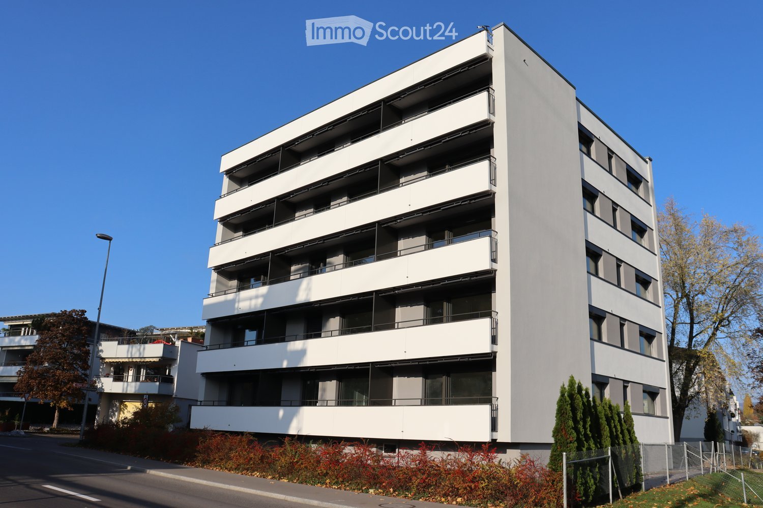 Modern multi-story apartment building with white facade, multiple balconies, and contemporary design.