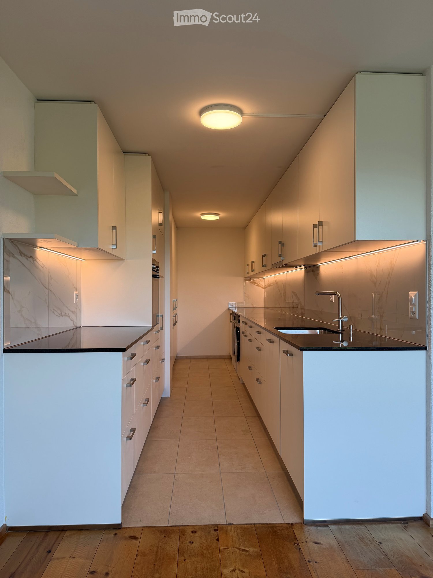 Modern kitchen with white cabinets, marble backsplash, wooden flooring, and built-in lighting.