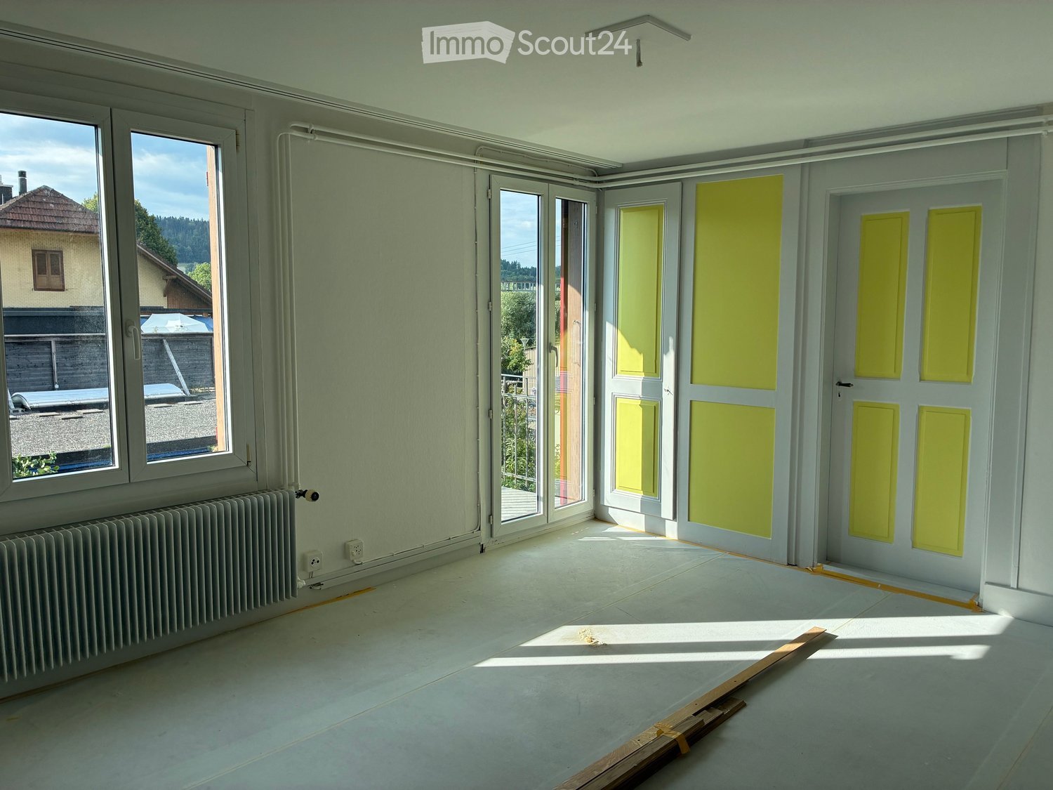 Empty room with light-colored walls, large windows, and a radiator. The space is unfurnished with no visible furniture or equipment.