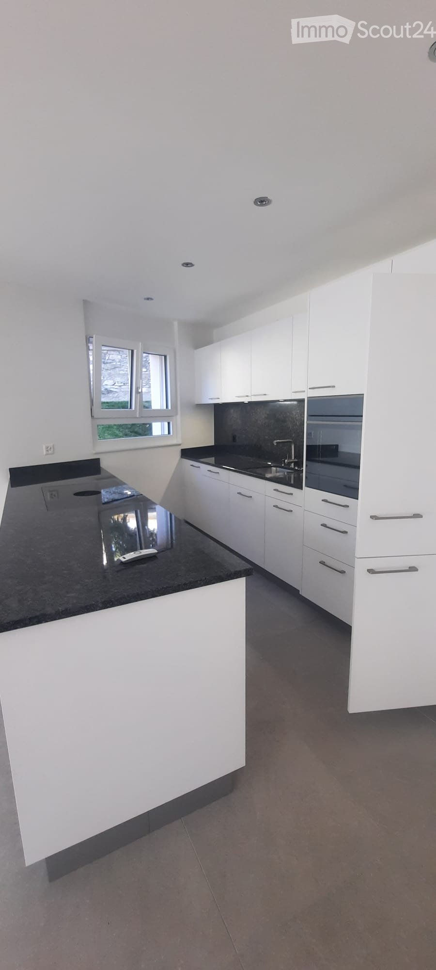 Modern kitchen with white cabinets, black countertops, and stainless steel appliances. Features a large window and a central island with a black countertop.