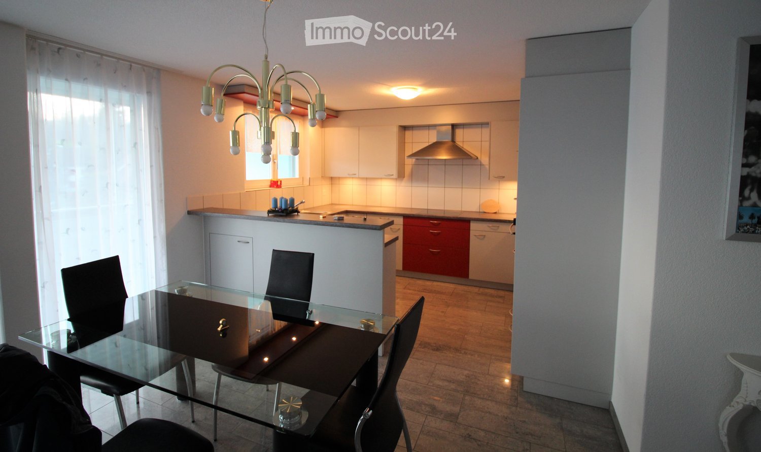 Modern open-plan living and dining area with a glass dining table, black chairs, white kitchen cabinets, red lower cabinets, and a central island.