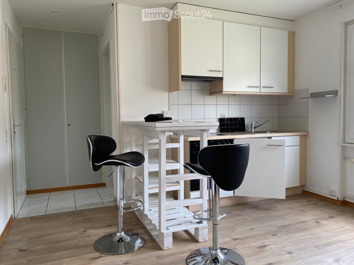 Modern kitchen with white cabinets, wooden flooring, a white island table, and two black bar stools.