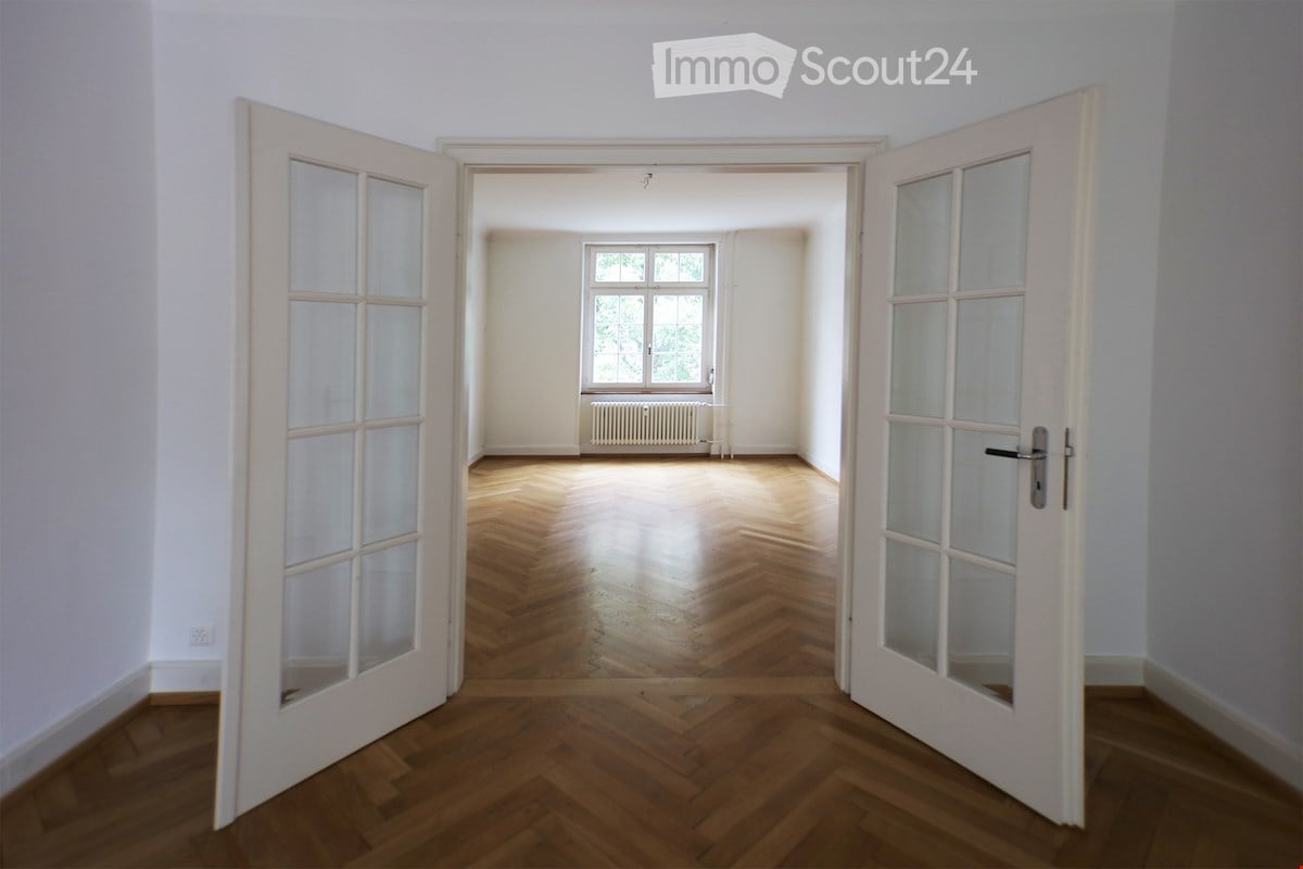 wood floor, white walls, radiator, two open doors, windows with a view