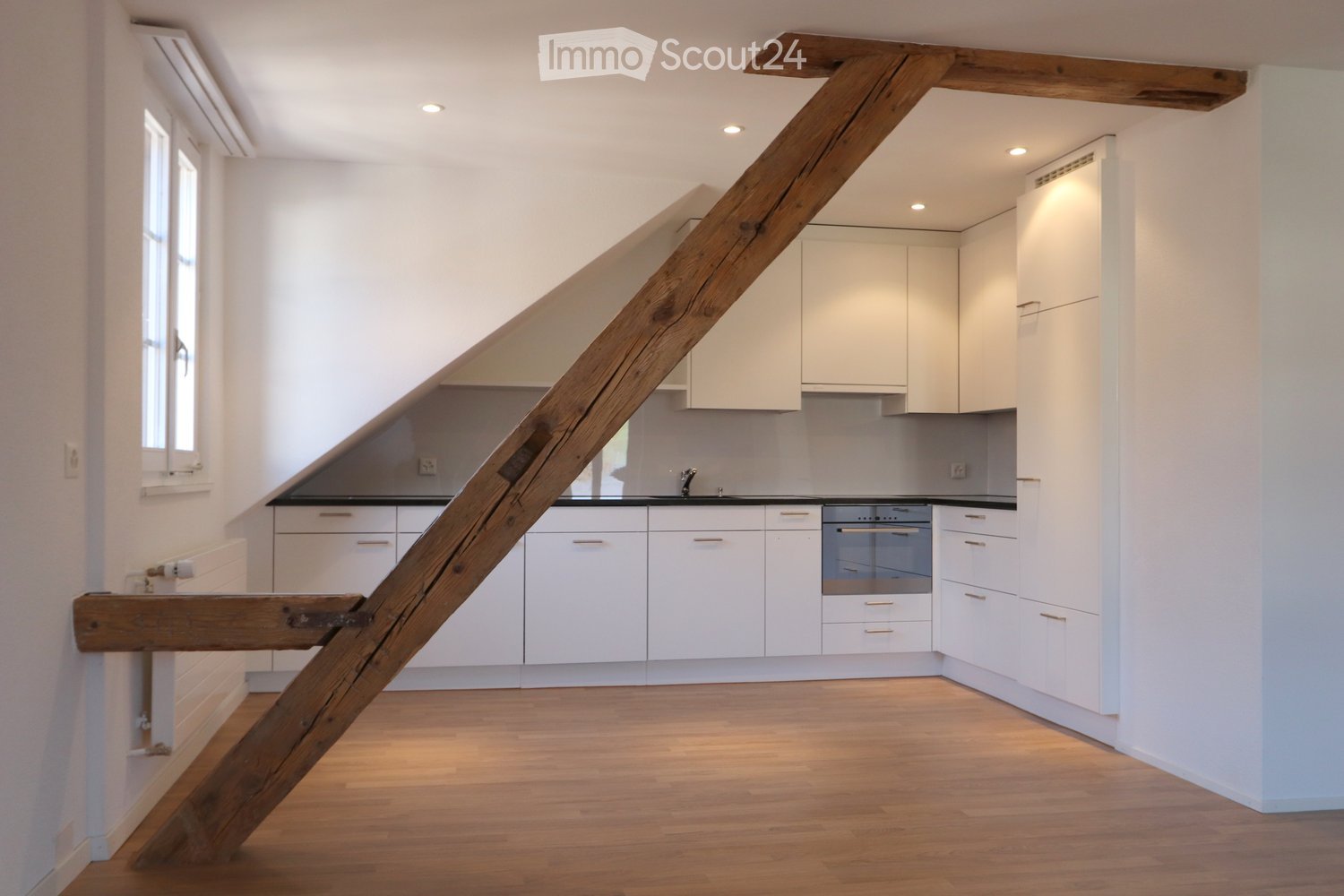 Modern kitchen with white cabinets, stainless steel oven, and wooden staircase leading to another level.