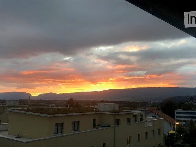 Balcony view overlooking a cityscape at sunset, with buildings and distant mountains visible.