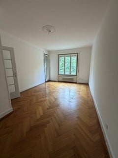 Completely empty room with wooden parquet flooring, white walls, and large windows with natural light. No furniture or equipment present.