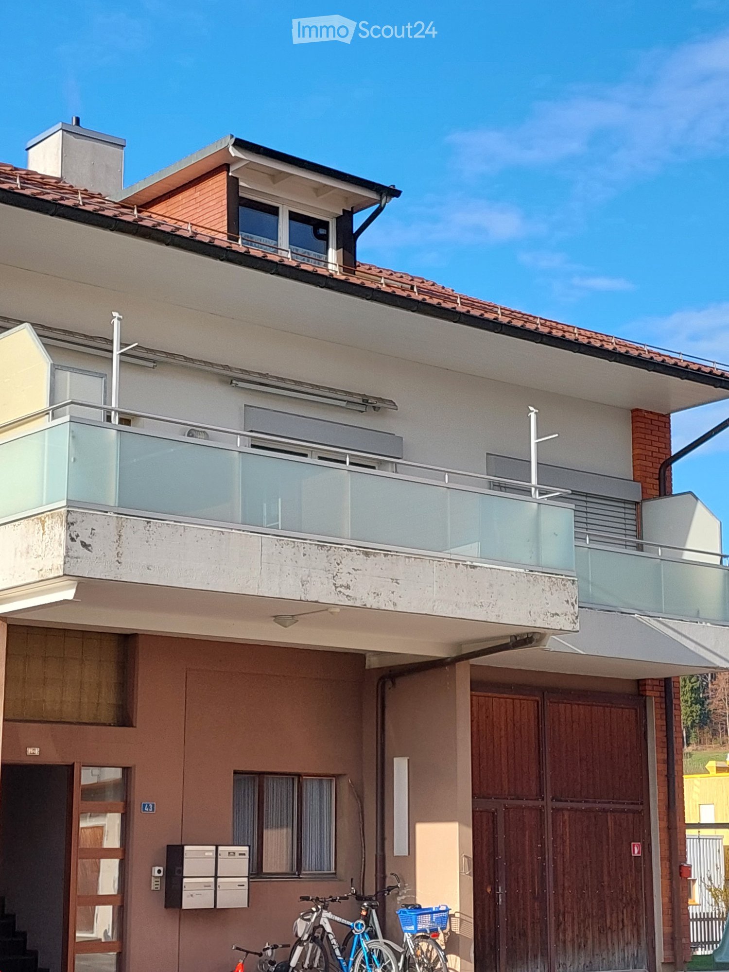 Two-story residential building with a balcony, wooden garage door, and bicycles parked in front.