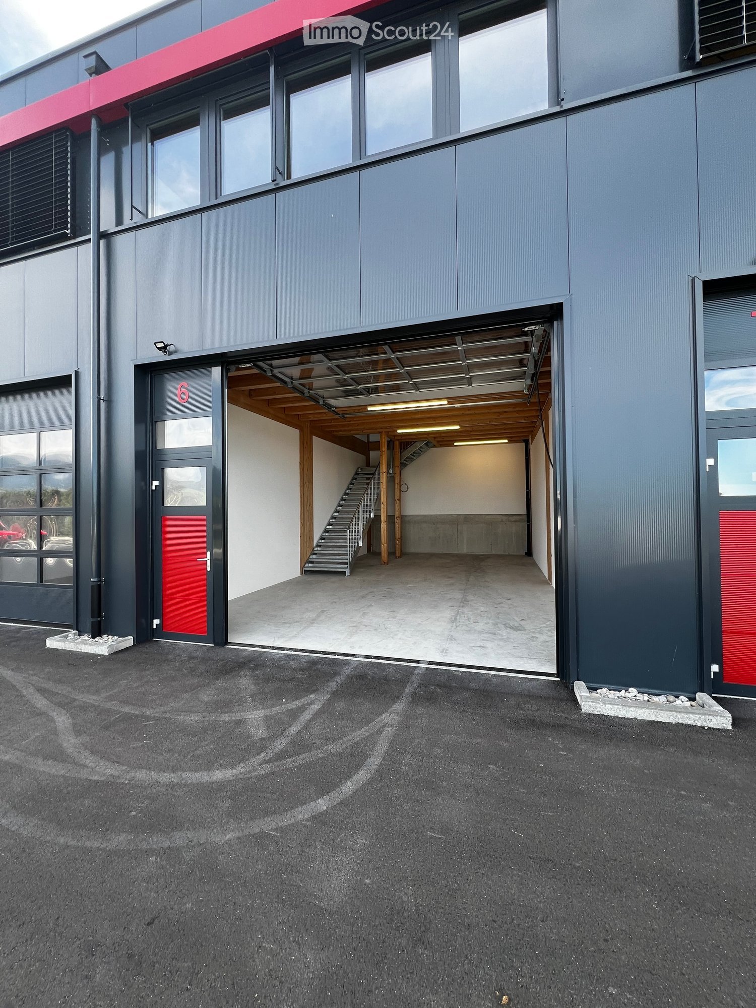 Modern two-story building with grey and red exterior, large windows, and a visible garage entrance with a staircase inside.
