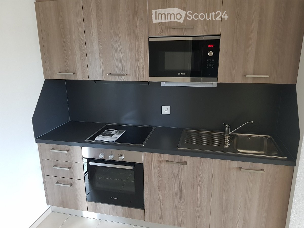Modern kitchen with light wood cabinets, stainless steel appliances, black countertops, and a built-in microwave and oven.