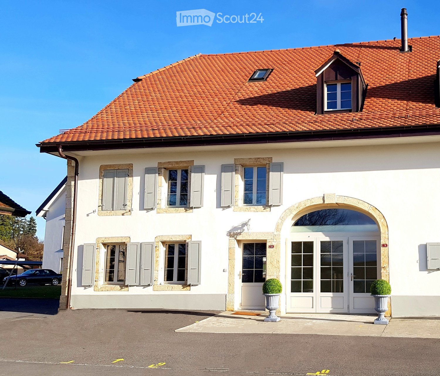 Two-story white house with red-tiled roof, multiple windows with shutters, arched entrance, and decorative planters.