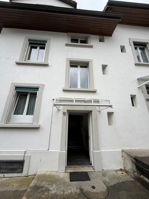 A multi-story residential building with white exterior walls, multiple windows, and a central entrance marked with the number 12.